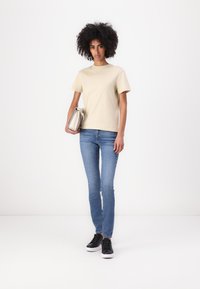 Beige cotton t-shirt with short sleeves, paired with light blue skinny jeans and black sneakers. Holding a silver clutch bag.
