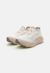 Zapatillas de running ligeras con una parte superior de punto blanca, acentos sutiles en rosa y una suela beige acolchada. Presenta una superficie texturizada y una suela exterior verde brillante.