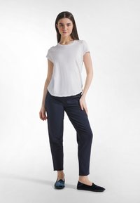 Camiseta blanca de manga corta, tejido suave, cuello redondo, combinada con pantalones ajustados azul marino y zapatos planos azul oscuro.