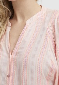 Blusa rosa chiaro con righe verticali in rosa scuro e arancione, con bottoni davanti, tessuto testurizzato e colletto alla coreana.