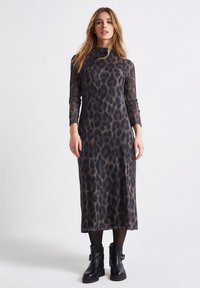 Midi sukienka w panterkę z długimi rękawami, wysokim dekoltem i dopasowanym krojem. Noszona z czarnymi botkami za kostkę, wykonana z przezroczystego materiału.