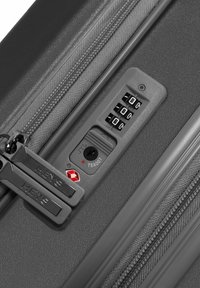 Grauer Koffer mit strukturierten Oberflächen. Verfügt über ein Zahlenschloss, markierte Reißverschlussanhänger und einen TSA-zugelassenen Sicherheitsverschluss.