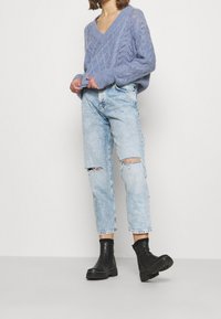 Maglione lavorato a maglia blu chiaro con scollo a V e motivi testurizzati, abbinato a jeans strappati chiari e stivali neri alla caviglia.