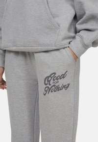 Graues Sweatshirt- und Jogginghosen-Set aus weichem Material. Die Hose hat den Schriftzug "Good for Nothing" in Dunkelgrau auf dem linken Oberschenkel.