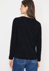 Maglione nero con texture, maniche lunghe, caratterizzato da un motivo sottile, scollo rotondo e vestibilità ampia. Indossato con denim blu casual.