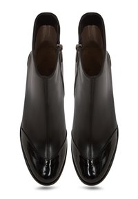 Bottines noires en cuir avec une finition lisse, présentant un bout en vernis noir brillant, une fermeture éclair sur le côté et un design arrondi.