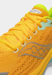 Φωτεινό πορτοκαλί παπούτσι τρεξίματος με κίτρινες κορδόνια, πλέγμα επάνω μέρος, αντανακλαστικό ασημένιο λογότυπο και νέον πράσινη εσωτερική επένδυση.