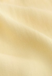 Weicher, hellgelber Stoff mit sichtbarer diagonaler Webstruktur und sanften Falten, die eine glatte Oberfläche schaffen.