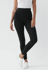 Zwarte leggings van rekbaar materiaal, met een hoge taille en een slanke pasvorm, gecombineerd met witte sneakers. Glad textuur overal.