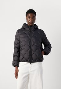 Melna pūkaina jaka ar quilted dizainu un kapuci. Ir priekšējais rāvējslēdzis un sānu kabatas. Gluda tekstūra un sportisks siluets.