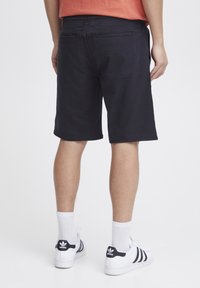 Marinblå shorts med en avslappnad passform, elastisk midja och två bakfickor. Bärs med vita sneakers och ankellånga strumpor.
