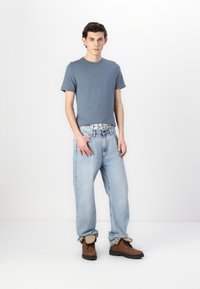 Lys blå bomull t-skjorte kombinert med løstsittende lys blå jeans og brune ankelstøvler. Jeansene har en synlig rutete midjeelastikk.
