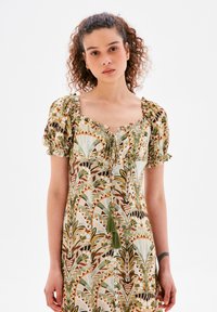Kleid mit Blumenmuster, Puffärmeln, quadratischem Ausschnitt und Vorderband. Hergestellt aus leichtem Stoff in Grün-, Beige- und Brauntönen.