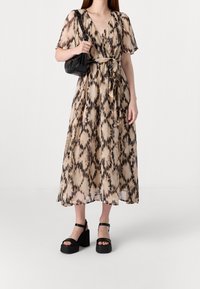 Vestido wrap beige con estampado animal, mangas cortas, un cinturón con lazo y una silueta fluida, combinado con sandalias negras de tacón ancho.