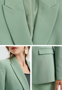 Ljusgrön blazer med skarpa slag, slät textur, en bröstficka och synlig sömnad. Inkluderar detalj av örhänge och mönstrad topp under.