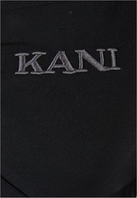 Tissu noir ajusté avec l'inscription "KANI" brodée en fil argenté. Texture lisse avec un léger brillant, mettant en valeur le détail du logo.