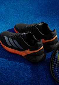 Μαύρα αθλητικά παπούτσια με πορτοκαλί λεπτομέρειες και υφασμάτινους άνωρους με υφή, με τρεις ανακλαστικές ρίγες και σχεδίαση με μαλακή σόλα.