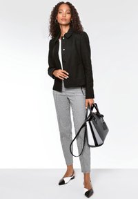 Zwarte cropped jas met een knoopsluiting, gecombineerd met zwart-witte houndstooth broek. Houdt een zwart-witte handtas vast, draagt slingback schoenen.