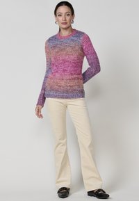 Mehrfarbiger Strickpullover in Pink-, Lila- und Blautönen, mit langen Ärmeln und Rundhalsausschnitt, kombiniert mit cremefarbenen, ausgestellten Hosen.