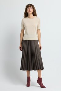 Cremfarbener Strickoberteil mit kurzen Ärmeln und rundem Halsausschnitt, kombiniert mit einem schokoladenbraunen, plissierten Midikleid und roten Stiefeletten. Glatte Textur, gestuftes Outfit.