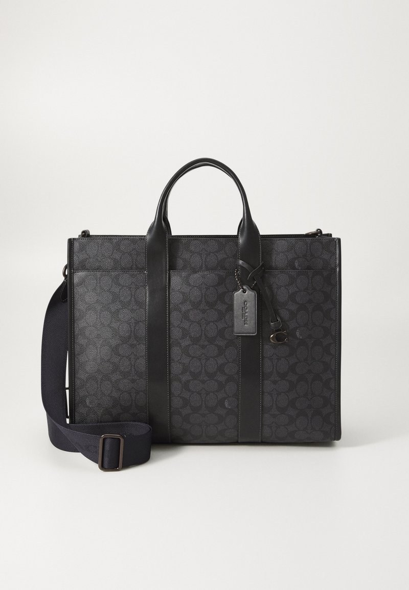 Black tote bag with textured fabric, leather accents, and two top handles. Features a removable shoulder strap and a hang tag.
