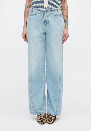 Lyseblå jeans med vid ben og snøre i taljen, med falmede pletter og syede sømme, kombineret med leopardmønstrede sko.