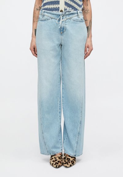 Lyseblå jeans med vid ben og snøre i taljen, med falmede pletter og syede sømme, kombineret med leopardmønstrede sko.