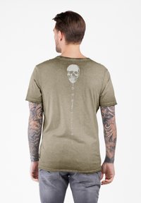 Camiseta de manga corta color verde oliva con un gráfico de calavera en blanco en la parte posterior. Textura suave y ajuste relajado con un dobladillo ligeramente desgastado.