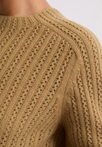 Garen trui in een warme beige kleur met getextureerde verticale strepen, voorzien van open patronen en een klassieke ronde hals.