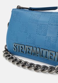 Blå tekstureret håndtaske med et præget logo, sølvhardware og en kraftig kædestrop. Lukning med lynlås.