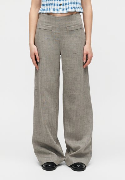Γυναίκα που φοράει γκρι παντελόνι με φαρδύ πόδι και ψηλή μέση, συνδυασμένο με μαύρα παπούτσια και κοντό μπλε-λευκό καρό τοπ.