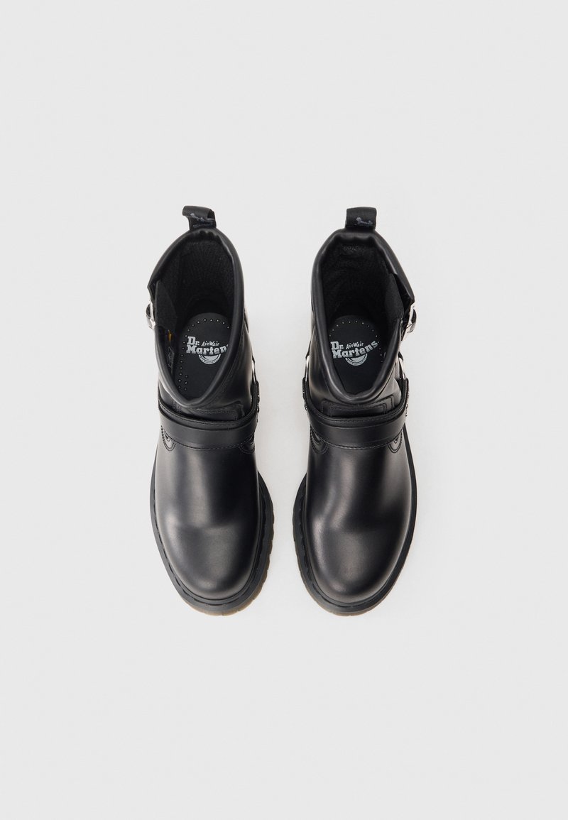 Schwarze Lederknöchelstiefel mit glatter Oberfläche, ausgestattet mit einem Riemen über der Vorderseite, einem gepolsterten Kragen und einer Zuglasche für einfaches An- und Ausziehen.