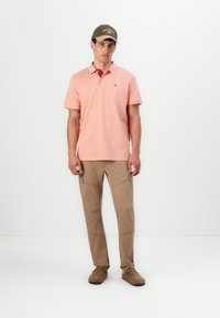 Helles rosa Poloshirt mit kurzen Ärmeln und einem Kragen, kombiniert mit tanfarbenen Cargo-Shorts, die mehrere Taschen und eine glatte Oberfläche aufweisen.