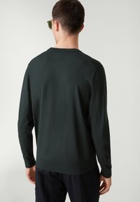 Pull à manches longues vert foncé, tissu texturé, col rond côtelé et poignets. Présente un ourlet droit sans motifs ni décalcomanies visibles.