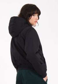 Schwarze Kapuzenjacke mit lockerem Schnitt, gerippten Bündchen und Saum. Hergestellt aus glattem Material, mit einem schlichten, modernen Design.