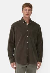 Brązowa koszula z korduroyu zapinana na guziki, z kołnierzykiem, pojedynczą kieszonką na piersi i zapięciem na guziki. Lekko teksturowany materiał, z długimi rękawami.