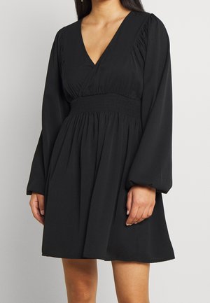 Robe noire avec un décolleté en V, manches longues bouffantes et taille smockée. Confectionnée dans un tissu léger avec une jupe fluide.