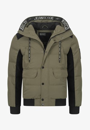 Olivengrønn pufferjakke med svarte kordfløyelsdetaljer, snorhette, glidelås, lommeposter og ribbestrikkede mansjetter. Strukturert overflate.