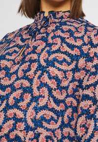 Blommig blus med volangkrage, som har en marinblå bas prydd med rosa och blå paisleymönster samt en nyckelhålsdetalj.