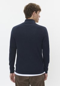 Temno modra polo majica z dolgimi rokavi, visoko ovratnikom in rebrastimi manšetami. Izdelana iz mehke tkanine, ima slim fit in majhen logotip na robu.
