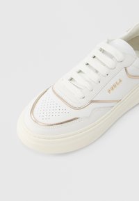 Λευκό δερμάτινο αθλητικό παπούτσι με μεταλλικές χρυσές λεπτομέρειες, διάτρητο μπροστινό μέρος και στρογγυλά κορδόνια. Το όνομα της μάρκας "Furla" είναι ανάγλυφο στο πλάι.