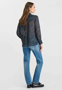 Long-sleeve, lightweight blouse in dark blue with an abstract pattern in orange and brown tones, paired with light blue jeans and black shoes.