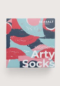 Boîte colorée pour chaussettes présentant un design abstrait graphique en rouge, rose, bleu et marine avec du texte blanc. Le nom de la marque est visible.
