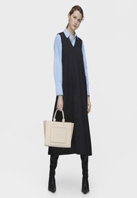 Czarna sukienka bez rękawów na niebieskiej koszuli z kołnierzykiem, w połączeniu z beżową skórzaną torebką z wytłoczonym logo. Czarnekozaki do kolan.