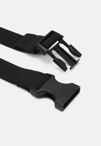 Primo piano di una cinghia nera in nylon regolabile con fibbia in plastica a rilascio laterale, non fissata, su sfondo bianco.