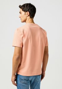 Vaaleanpunainen lyhythihainen t-paita pyöreällä kauluksella, sileä rakenne ja rento malli, yhdistettynä sinisiin farkkuihin. Ei näkyviä grafiikoita tai kuvioita.