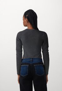 Gray long-sleeve cropped top with a soft texture, paired with black jeans featuring blue denim accent pockets and contrasting stitching.