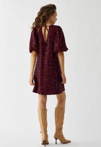 Rochie burgundy cu paiete, cu mâneci bufante și spate în V adânc, asortată cu cizme din piele bej până la genunchi, cu vârf ascuțit și toc stiletto.