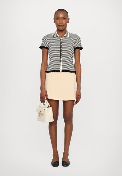 Blusa de rayas blancas y negras de manga corta con cuello y dobladillo rizado; falda beige; bailarinas negras; bolso pequeño blanco con herrajes dorados.