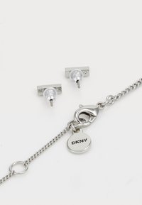 Orecchini a perno in argento con bead trasparenti, dotati di una base rettangolare e di un piccolo gemma trasparente. Include un bracciale in argento con chiusura.